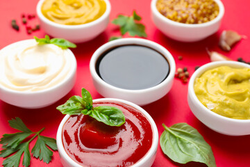 Different sauces, spices and herbs on red background, closeup