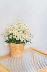 Artificial flowers in pots sit on a table next to a white wall.