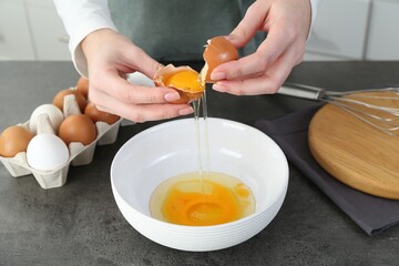 Woman cracking egg into bowl at grey table in kitchen, closeup