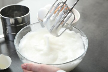 Woman beating egg whites with mixer at grey table, closeup