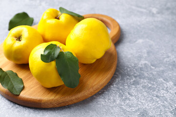Ripe quinces and green leaves on grey table, closeup. Space for text