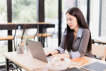 Asian young woman intently focusing and typing on a laptop computer, working remotely from a modern office or coffee shop environment, embodying business, finance, and career concepts