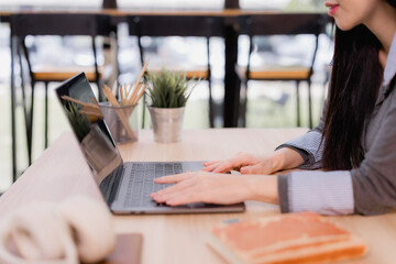 Woman's hands are actively typing on a modern laptop keyboard, focusing on her work while sitting at a light wooden desk in a contemporary co-working office space