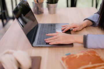 Woman hands are actively typing on a laptop keyboard and using the trackpad, performing tasks on a wooden desk in a bright office environment, illustrating productivity and modern remote work