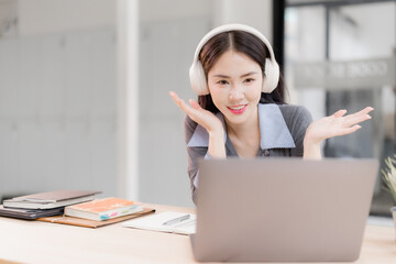 Woman wearing headphones smiles while looking at her laptop screen, actively participating in an online video conference or remote work meeting from a modern office setting