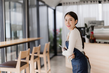Woman barista wearing an apron smiling and holding a digital tablet in a modern coffee shop, symbolizing small business ownership, entrepreneurship, and customer service