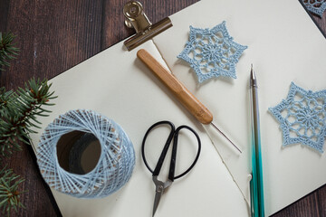Crochet yarn, hooks and scissors arranged for making lace snowflake ornaments. Handmade Christmas decor and eco-friendly winter craft concept.