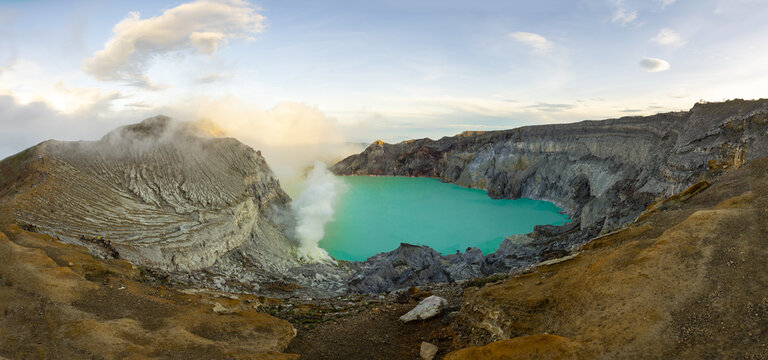 View of a vibrant turquoise lake nestled within a volcanic crater, surrounded by rugged terrain with steam rising into the sky, Banjuwangi, East Java, Indonesia.