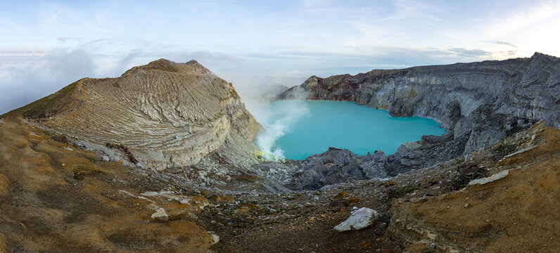 View of a vibrant turquoise lake nestled within the imposing volcanic landscape, surrounded by rocky cliffs and sulfur deposits, Banjuwangi, East Java, Indonesia.