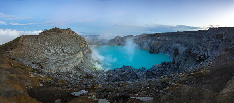View of the electric blue crater lake nestled within the rugged, smoky landscape of Ijen volcano, a geological wonder, Banyuwangi, East Java, Indonesia.