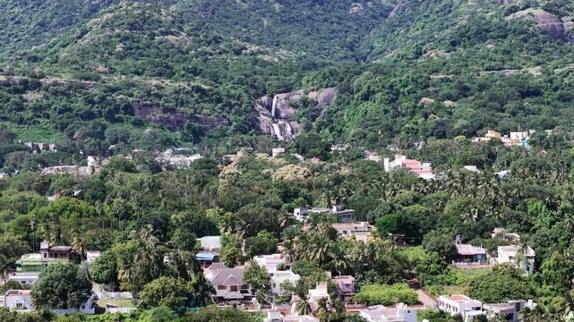 Stunning aerial view of Courtallam Main Falls in Tamil Nadu in the South Indian hills, flowing into a town surrounded by a lush green forest. Ideal for travel, nature, and tourism-related content.