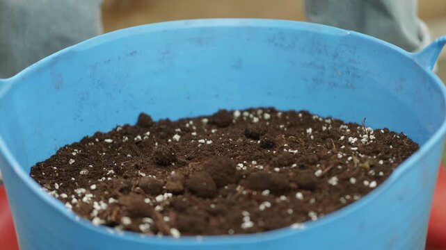 A blue container drops into frame that holds dark soil mixed with perlite, ideal for starting seeds. This setup prepares for planting in a spring garden.