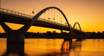 Obraz premium Arched bridge over reflective water at sunset, orange sky backdrop