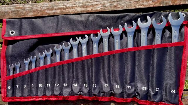 Full set of combination spanner wrenches in a roll bag lying on a wooden bench. Various sizes of mechanical tools for repair.