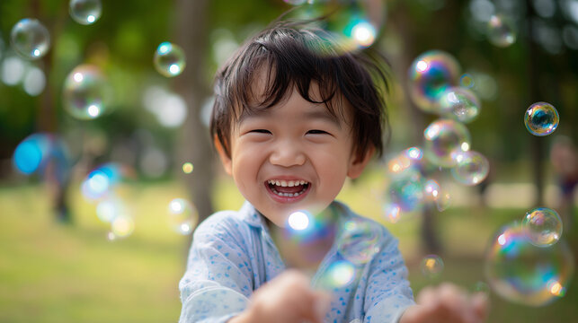 Happy young 4-year-old toddler of asian boy playing with bubbles outdoors in the park   - Powered by Adobe