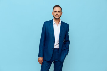 Businessman in a navy suit stands confidently against a solid blue backdrop, conveying professional poise, focus, and calm determination in a clean studio setting.