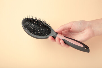 Woman hand holding hairbrush on beige background.