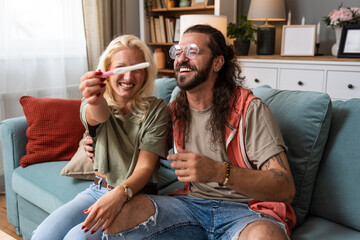 Happy couple celebrating a positive pregnancy test at home joyful announcement, emotional smiles,...