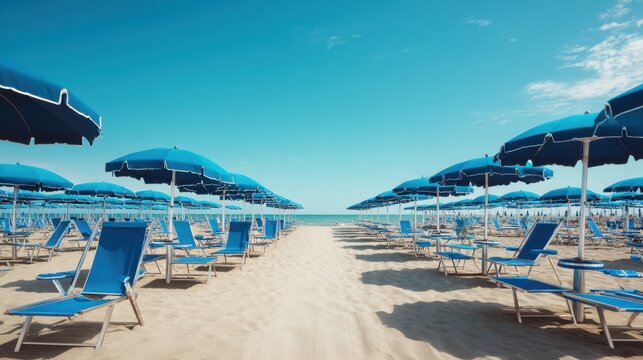 Rows of blue beach umbrellas and lounge chairs on a sandy beach. Summer vacation and travel destination concept for holiday brochures.