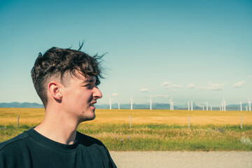 A man standing against a backdrop of serene wind turbines and a blue sky.