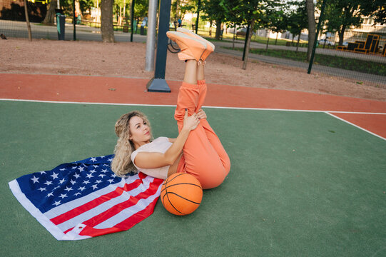 Woman stretching on court over USA flag, basketball near feet. Active lifestyle, mobility and warm-up concept.