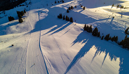 Aerial view of a snowy mountain slope at sunset with long shadows