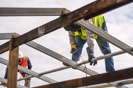 Construction Workers Welding Steel Beams at a Job Site Under a Partly Cloudy Sky in Daylight