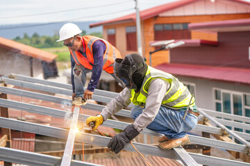 Construction Workers Engaged in Metal Roof Installation with Safety Gear on a Sunny Day at a Building Site in Focused Action