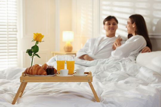 Tray with delicious breakfast on bed and happy couple enjoying their stay at hotel room, selective focus