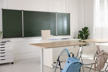 Green chalkboard, backpacks and stylish furniture in classroom. Mockup for design