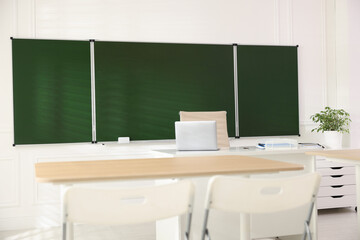 Green chalkboard and stylish furniture in classroom. Mockup for design