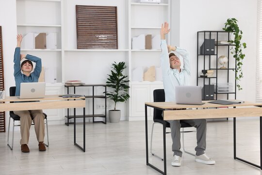 Man and woman doing stretching exercise in office - Powered by Adobe