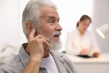Senior man with hearing aid and doctor working in hospital, selective focus