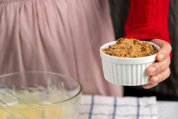 Close-up of a person holding a ramekin filled with brown sugar, ready for holiday cookie baking