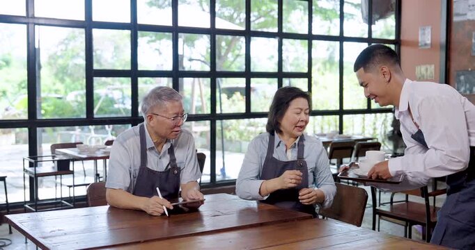 Elderly asian entrepreneur couple restaurant owner talking at cafe table using tablet teamwork communication cooperation lifestyle partnership management barista serving coffee teamwork collaboration