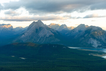 Fototapeta premium Stunning mountain range under a cloudy sky, green forest in the foreground.