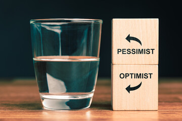 Glass of water with wooden blocks labeled optimist and pessimist symbolizing positive and negative mindset, attitude perspective, and psychological concept of optimism and pessimism