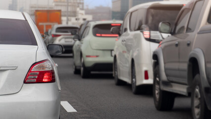 Rear side of white car with turn on brake light. Traffic of many car on the asphalt road parking is jammed in a row. Blurred background of town under light sky.