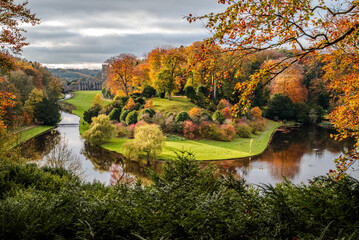 Obraz premium Autumn landscape from a viewpoint at Fountains Abbey, with trees glowing in warm fall colors under soft light and the abbey partially visible within the scenic vista - 1