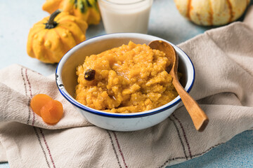 Pumpkin squash porridge with dried apricots and raisins on blue background with pumpkins