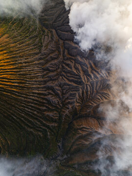 Aerial view of a dramatic landscape where earthy tones meet ethereal clouds near Mount Bromo, East Java, Indonesia.
