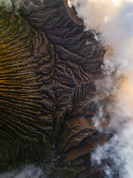 Aerial view of the rugged, textured terrain of Mount Bromo, with clouds clinging to its slopes, East Java, Indonesia.