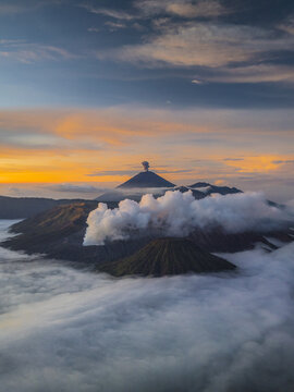 Aerial view of the majestic Mount Bromo shrouded in ethereal clouds, its peak piercing the vibrant sunrise sky, East Java, Indonesia.
