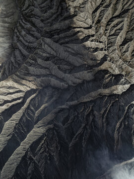 Aerial view of a volcanic landscape, the rugged terrain unfolding in shades of grey and brown, sculpted by time and the elements, Mount Bromo, East Java, Indonesia.