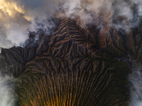 Aerial view of a rugged landscape with contrasting light and shadow, enveloped by ethereal clouds, Mount Bromo, East Java, Indonesia.