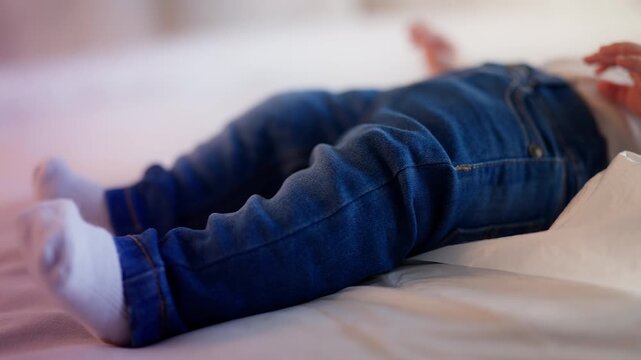 Close-up of infant in denim pants and socks lying on bed, moving tiny hands