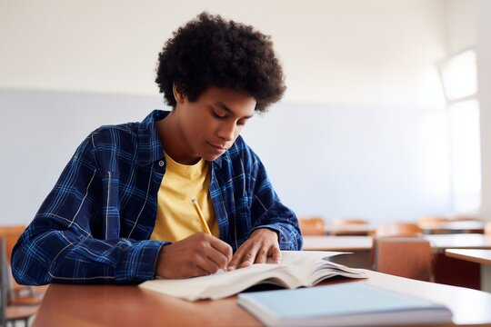 Focused teenage student writing in notebook during class. Education, learning, academic success, and dedication. Great for school, tutoring, online learning, and back to school themes.