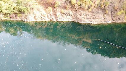 Aerial view of a small lake surrounded by rocky cliffs and autumn forest