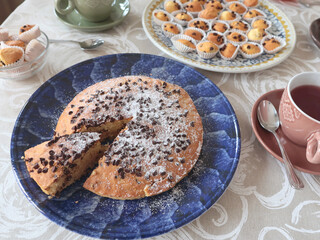 Chocolate chip cake on patterned ceramic plate. Holidays and lifestyle. Food on table covered with tablecloth. 