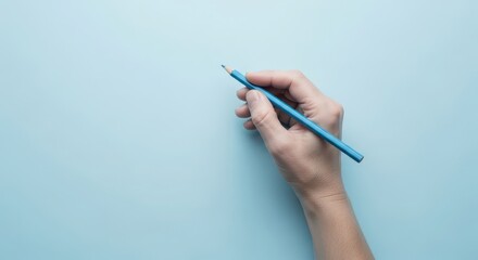 Top view of a hand holding a blue pencil on a matching blue background. A minimalist concept for creativity, art, and education